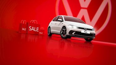 A white Volkswagen Polo against a bold red background, surrounded by red sale shopping bags.