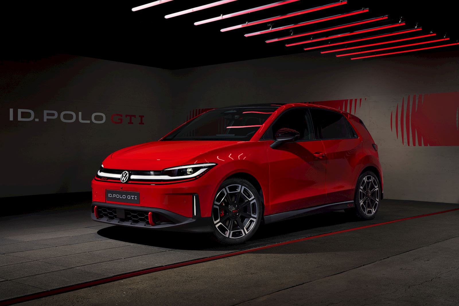 Volkswagen ID. Polo GTI concept car in Tornado Red, shown in a dramatic studio setting with red neon lighting overhead.