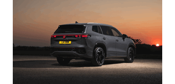 A dark silver Volkswagen Tiguan viewed from the rear in the dusk, with rear lights on